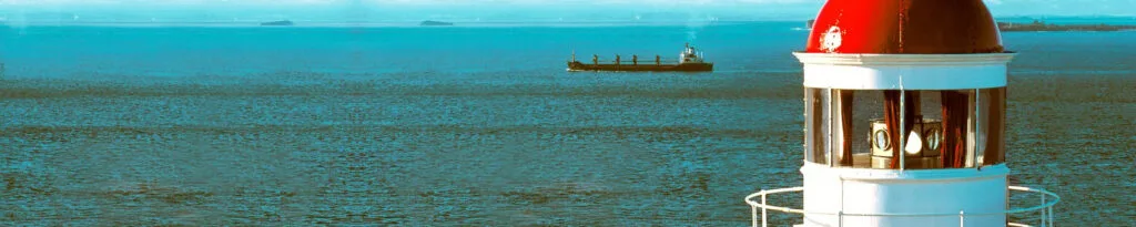 Faro junto al mar con un buque en el horizonte